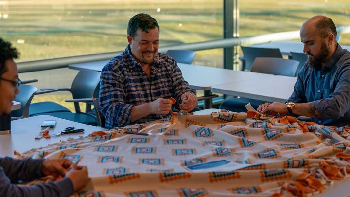 Employees participate in a group volunteer activity, working together to create a handmade fabric item in a collaborative workspace.