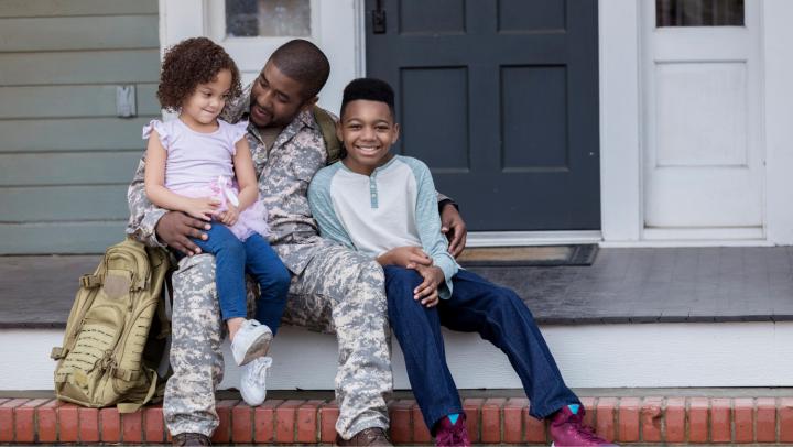 Adult seated on a front porch with two children, illustrating family support and housing stability.