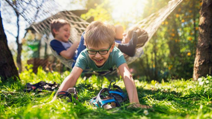 Children playing outdoors in a sunlit backyard, with one child crawling through the grass while others play in the background.