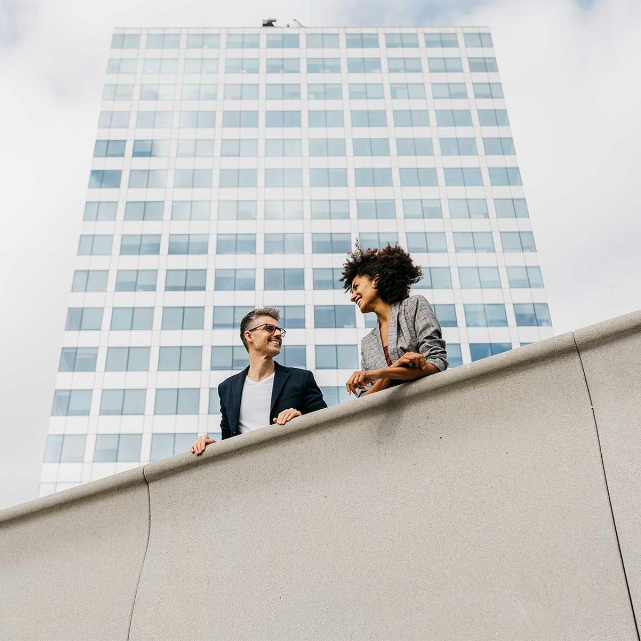 Two people talking in front of a skyscraper